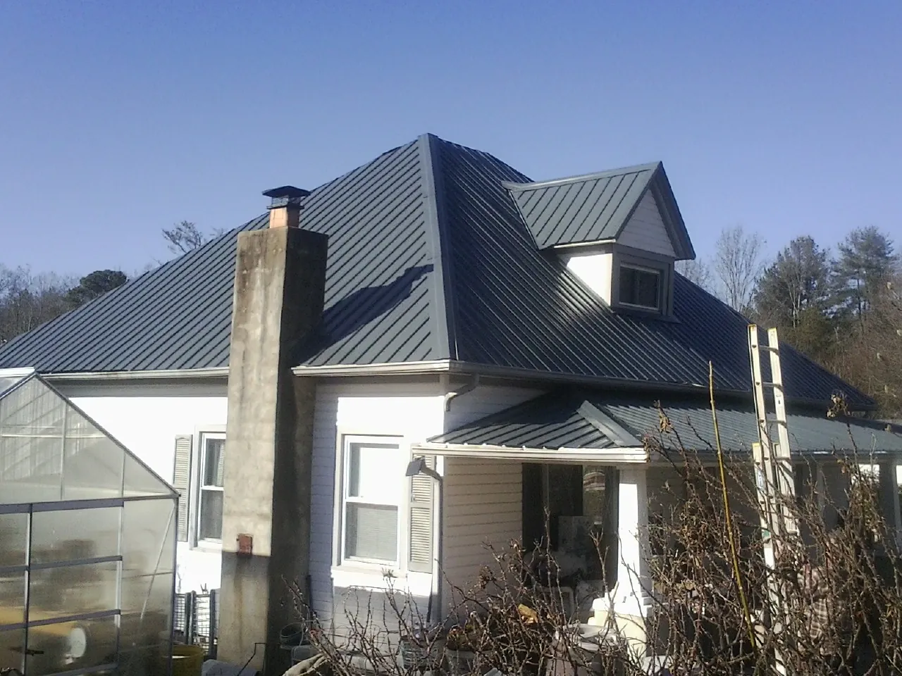 Dark blue standing seam metal roof on a white farmhouse with dormer — Slate & Tile Roof Repair by Roofing Brothers in Baxter Springs