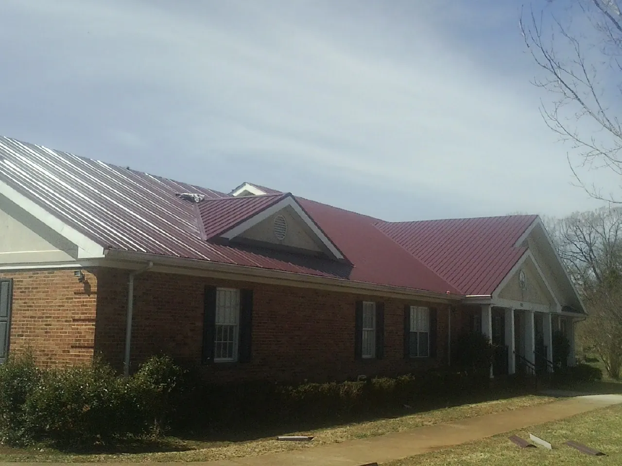 Red metal roof with gabled entries on a long brick building, from a Hail Damage Roof Repair job in Baxter Springs