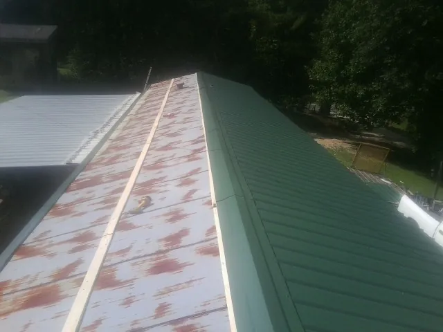 Old rusted panels beside newly installed green metal roofing — Wind Damage Roof Repair by Roofing Brothers in Baxter Springs