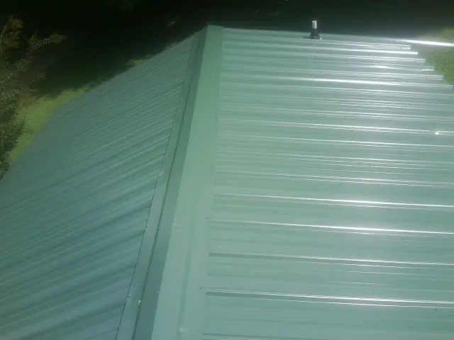 New green metal panels meeting at the ridge of a roof — Flat Roof Repair work by our crew in Baxter Springs