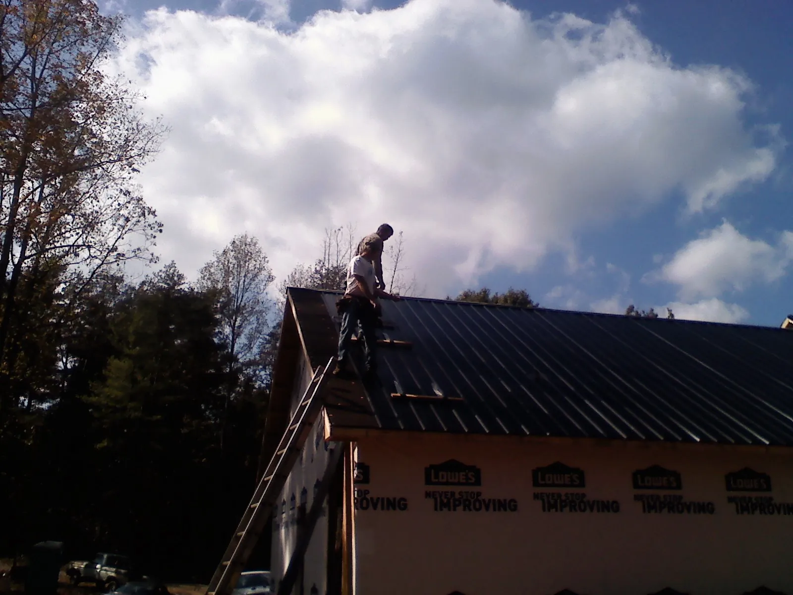 Roofer fastening dark metal panels high against a cloudy sky, from a Roof Inspection job in Baxter Springs