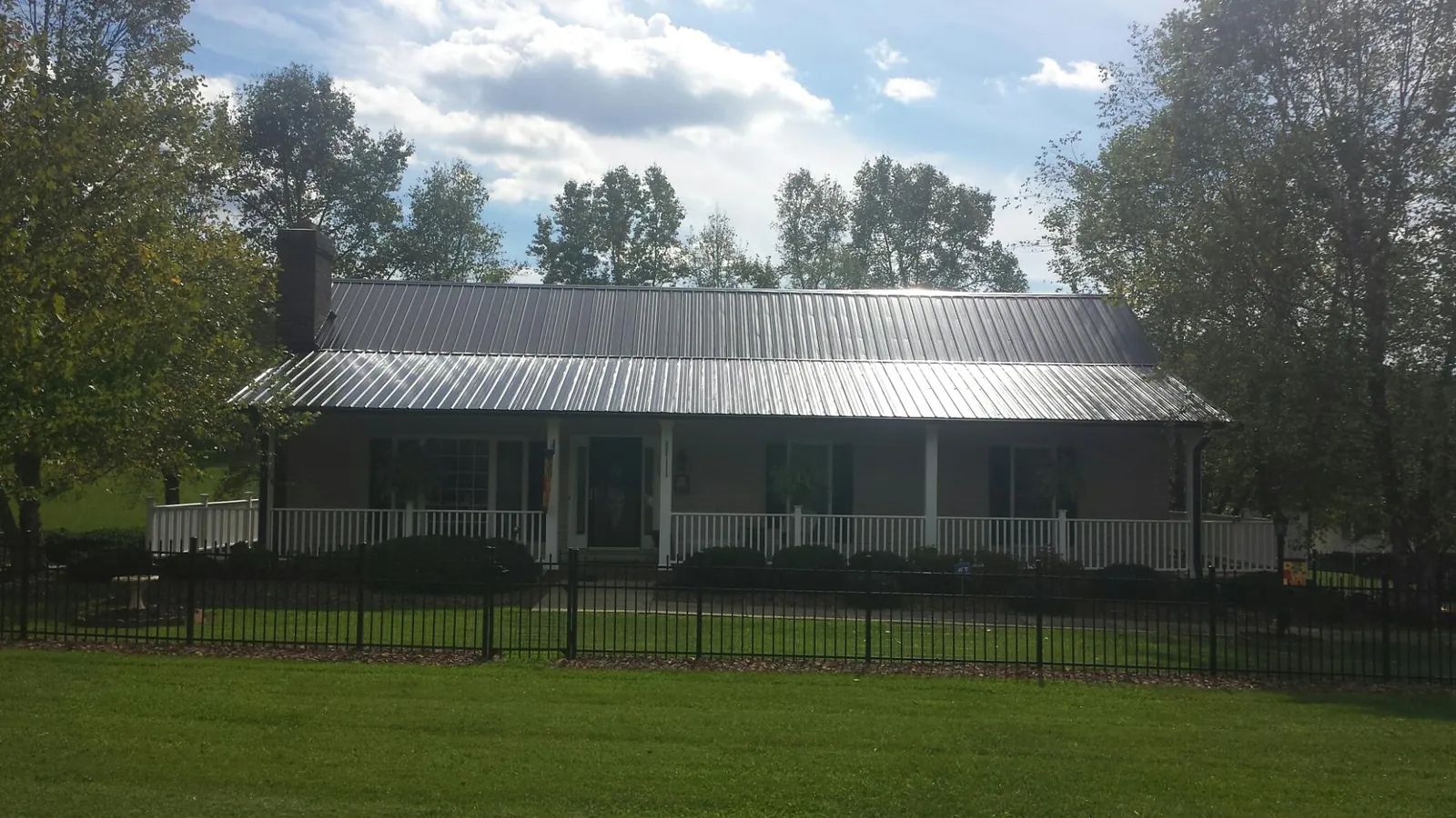 Gray metal roof on a brick ranch with a full width front porch — Gutter Guard Installation work by our crew in Baxter Springs