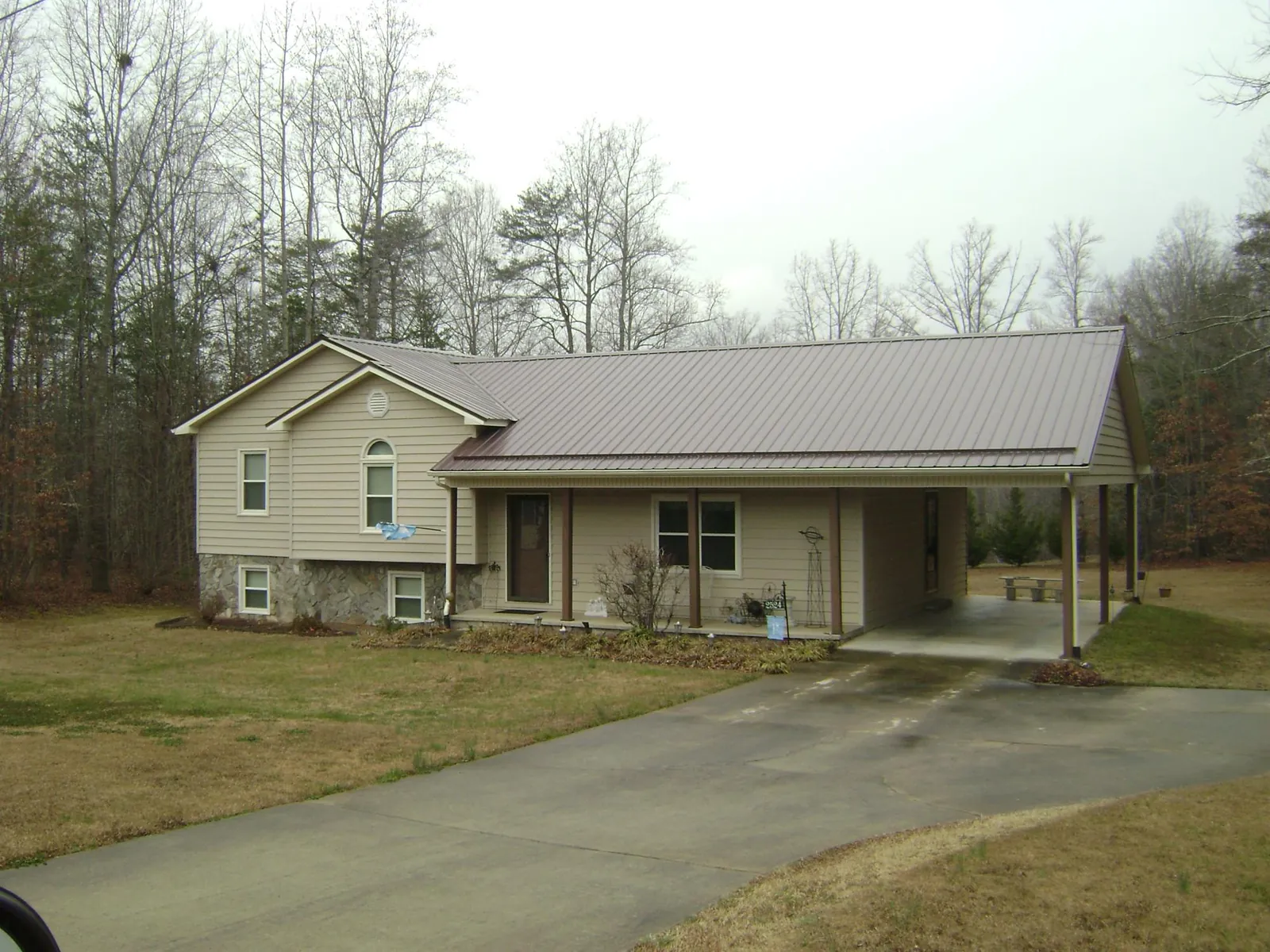 Brown metal roof on a tan split level home with an attached carport in Baxter Springs