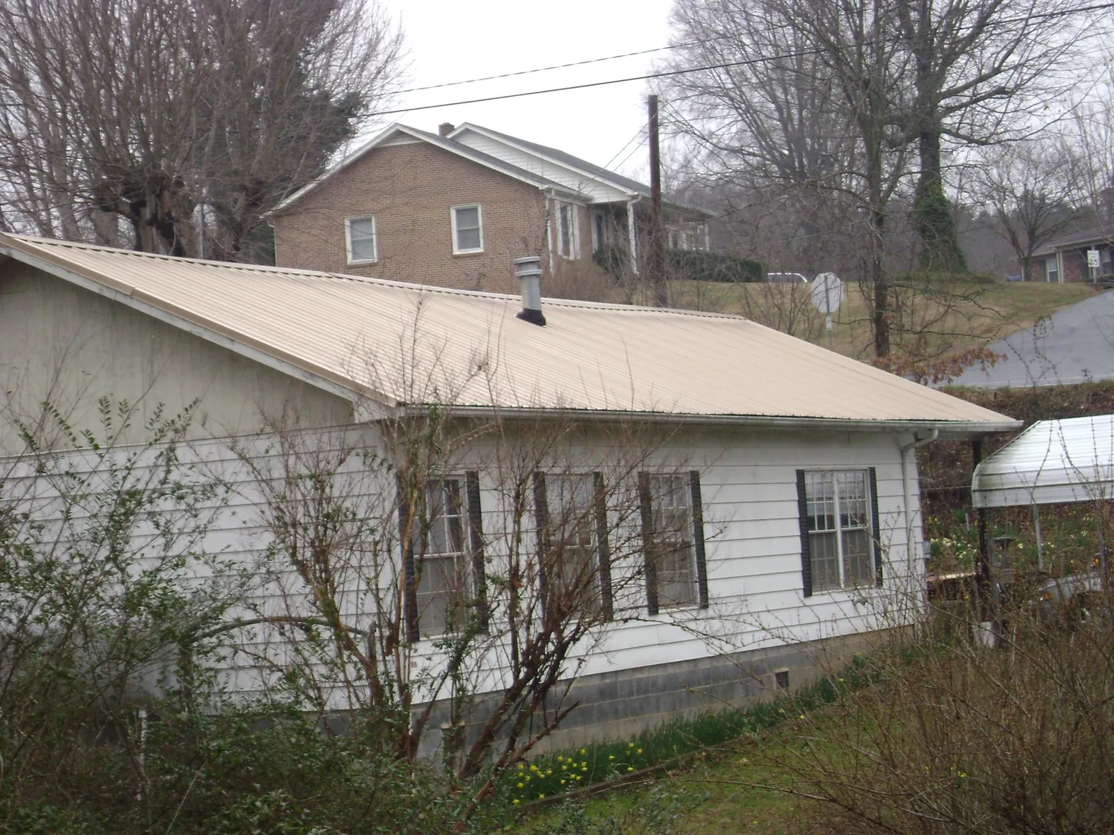 Tan metal roof on a white sided house set into a hillside — Commercial Roofing by Roofing Brothers in Baxter Springs
