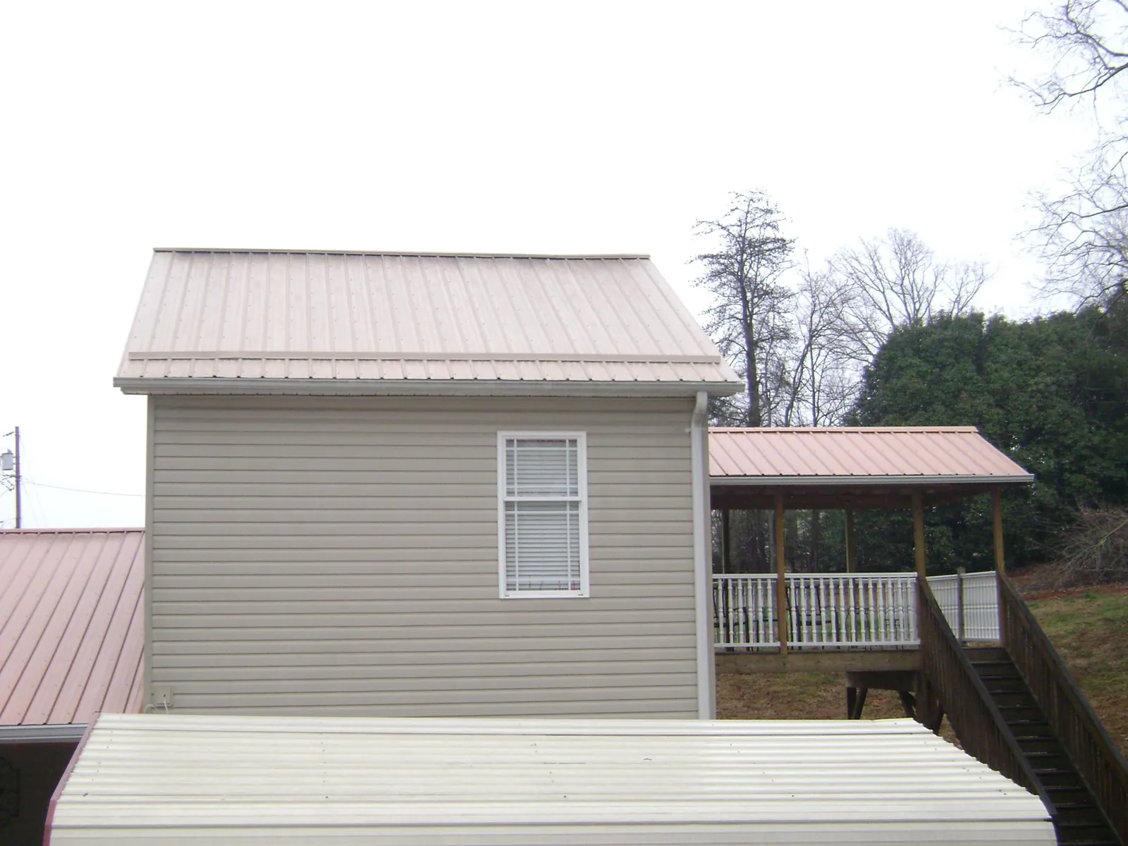 Tan metal roofs on a two story addition and attached porch, from a Roof Replacement job in Baxter Springs