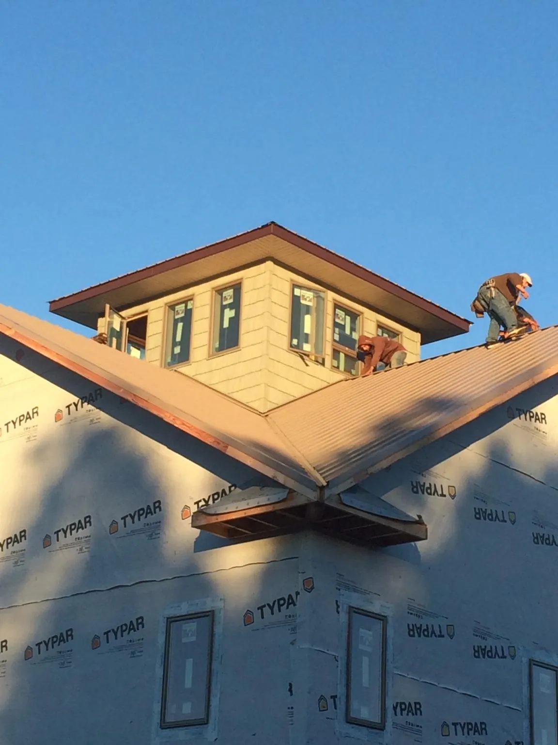 Roofers working around a rooftop cupola on a new metal roof at sunset — Roof Waterproofing in Baxter Springs by Roofing Brothers